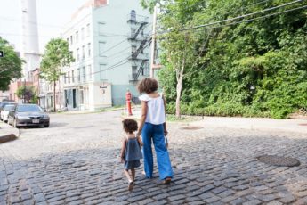 A woman walks with her third culture kid in the street.